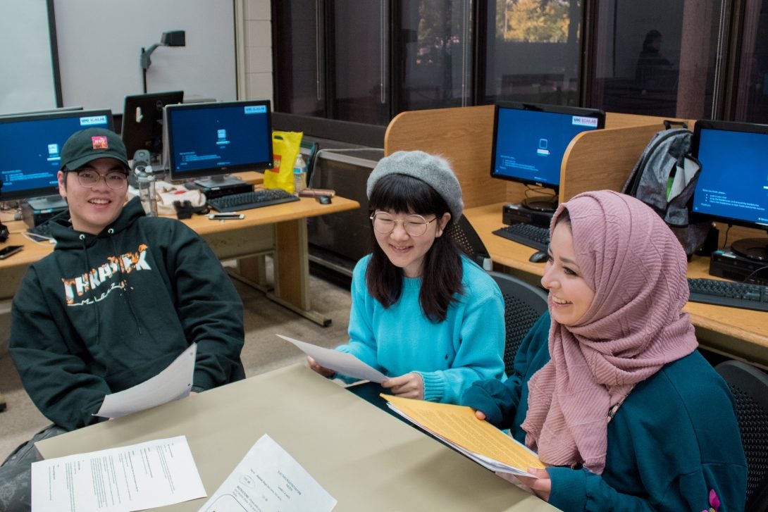 three students sitting at a table in a classroom